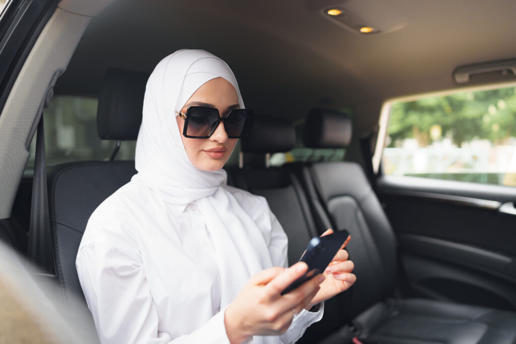 UMRAH IN RAMADAN : REWARDS, TIPS & BEST TRAVEL GUIDE 2025 2 beautiful muslim woman wearing white hijab sitting back seat car using smartphone